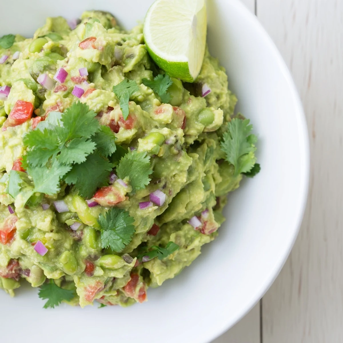 Creamy, bright green Edamame Guacamole, a vibrant dip, speckled with red onion and tomato.