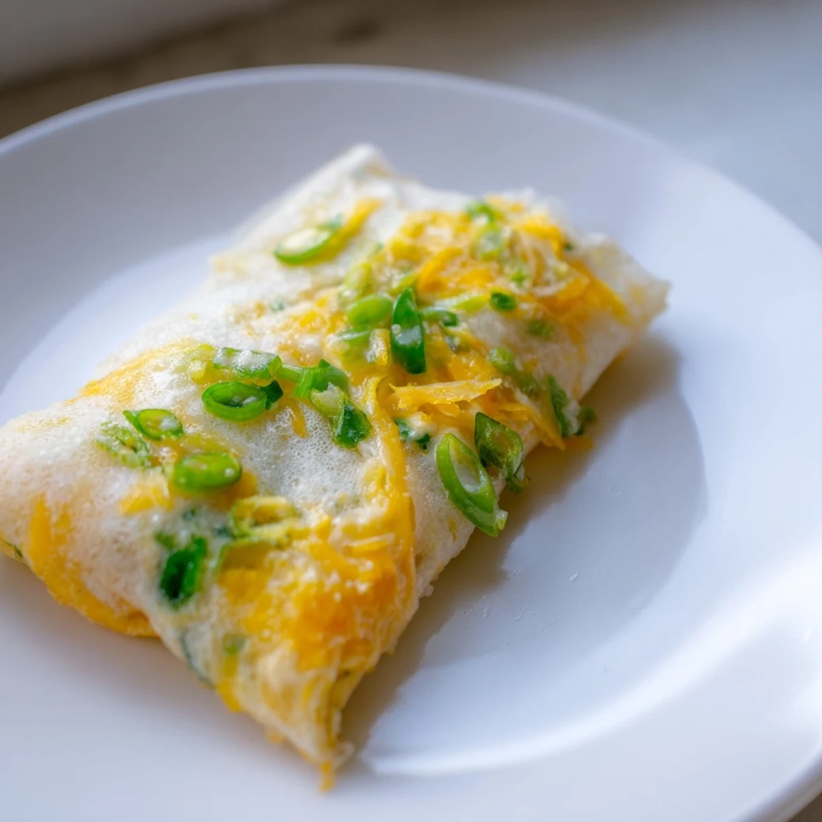 Melted cheese peeks out of a pan-fried Rice Paper Egg & Cheese Fold, ready to serve with sriracha.