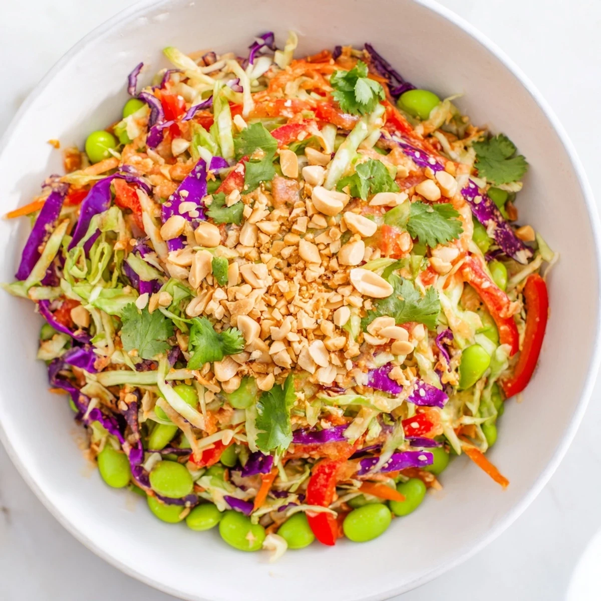 A vibrant bowl of Crunchy Thai Peanut Salad topped with chopped peanuts and lime wedges, perfect for a light lunch or potluck side. 