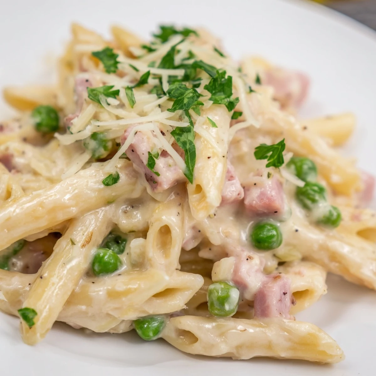 A steaming bowl of Spring Pea & Ham Pasta, with tender penne coated in a creamy sauce and dotted with bright green peas and savory diced ham.