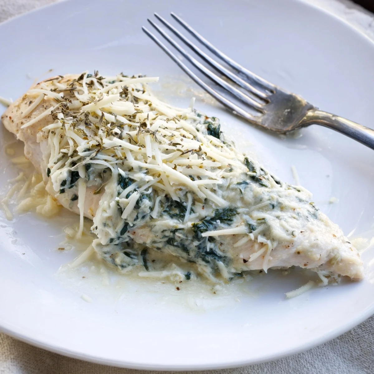 The baked spinach and artichoke chicken bake features golden, bubbly cheese topping on tender breasts in a white baking dish.