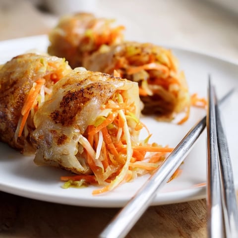 Golden-brown Crispy Rice Paper Dumplings resting on a white plate, filled with savory chicken and vegetables, served with a small bowl of tangy dipping sauce.