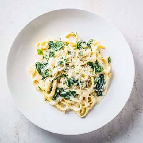 Creamy Garlic Spinach Pasta served in a white bowl, garnished with fresh parsley and a sprinkle of Parmesan cheese.