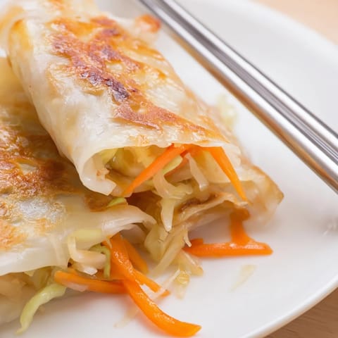 A close-up of a split Crispy Rice Paper Dumpling revealing its juicy cabbage and carrot filling, paired with chopsticks and a drizzle of spicy soy glaze.
