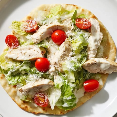 A close-up of a Chicken Caesar Flatbread garnished with shaved parmesan and halved cherry tomatoes on a rustic board.