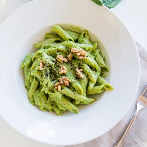 Freshly blended Creamy Spinach Walnut Pasta in a white bowl, garnished with toasted walnuts, lemon zest, and black pepper.  