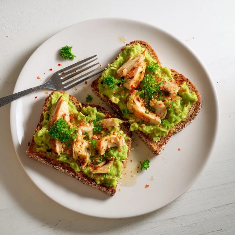 A close-up of the vibrant Smashed Avocado Chicken Toast, showcasing perfectly grilled chicken and fresh herbs on rustic bread with a drizzle of honey.